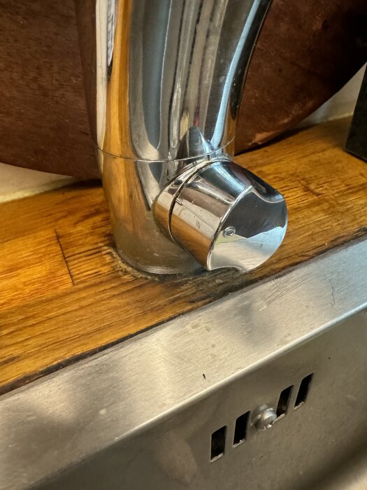 Kökshandfat med en kromblandare och fuktskadad träyta runt basen. Teppanytan och diskhons fog syns i närbild.