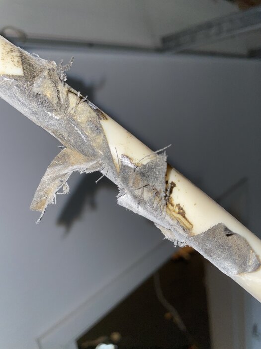 Ett vitt plast- eller PVC-rör med gråfärgad isolering eller smuts fastklistrad runt rörens yta.