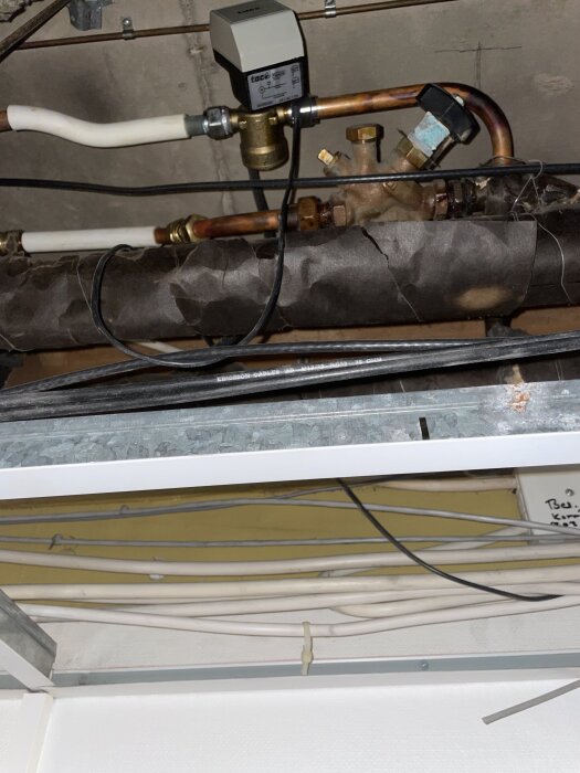 Rör med isolering och kablar i ett kontor under rivning, med fokus på isoleringens utseende kring ett PVC-rör.