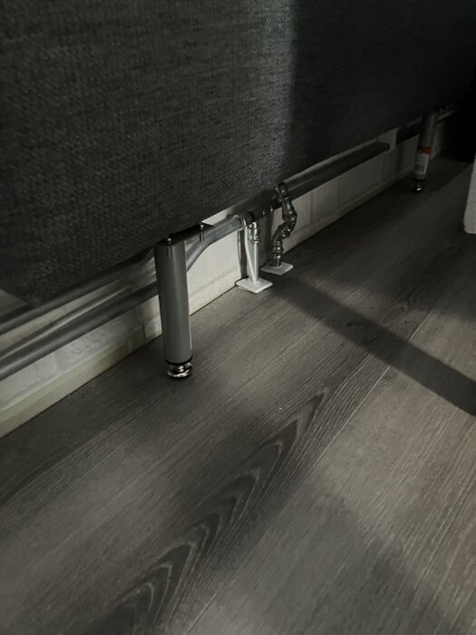 Möbelben och radiatorrör under en säng, monterat för att tillåta rörelse och undvika kontakten med golvbeläggningen.