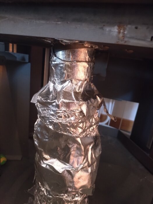 Ett rör täckt med metalltejp inuti en kamin, eventuellt relaterat till kaminsäkerhet och värmeskydd.