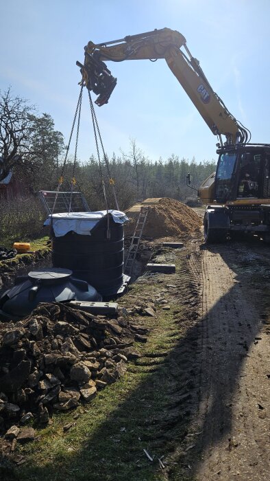 Grävmaskin installerar tank i utgrävd grop med kalksten runtom, del av slamnedbrytningssystem.