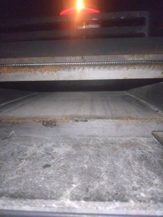 Asklådeutrymme i en kamin med ljus ovanpå och synlig spjällmekanism underifrån tilluftsröret.