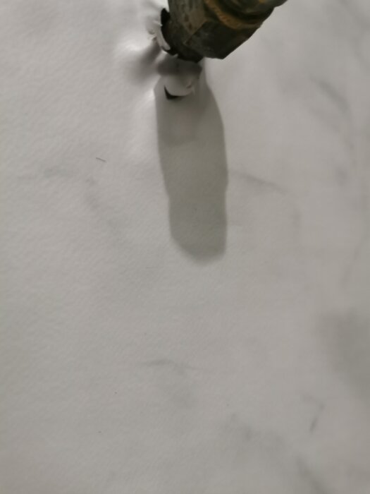 En ojämn montering av badrumsmatta runt ett rör, visar veck och skärningar i mattan.