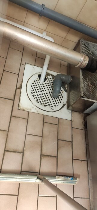 Golv med avloppsbrunn och ett grått plaströr som leder ut vatten på ett industriellt kaklat golv.