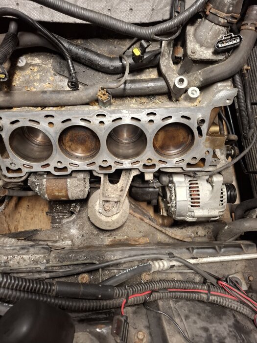 Bild av en motor med exponerade cylindrar och kablar, visar en del av en bilmotor under arbete eller service.