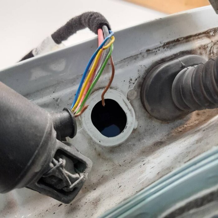 Flera kablar, inklusive en brun avbruten, syns intill en vit metallkant och gummitätningar i bilens interiör.