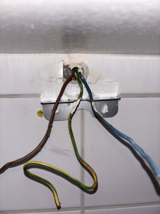 Elektriska kablar i ett badrum, exponerade och lösa kopplingar över kakel, potentiella elektriska problem.