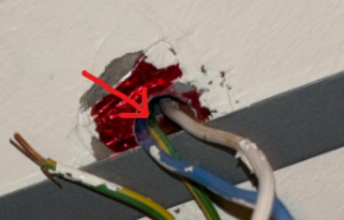 Elektriska kablar går in i ett hål i väggen, markerat med en röd pil. Det är osäkert om det finns en skada eller endast skugga.