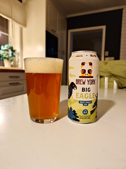 Ett glas med skummande öl och en burk Brew York Big Eagle West Coast IPA står på ett bord i ett kök.