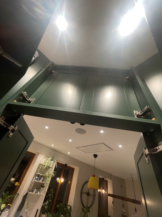 Grön skåpsram monterad på täcksidor till kyl och frys, med öppna dörrar och insidan som vetter mot taket i modernt kök.