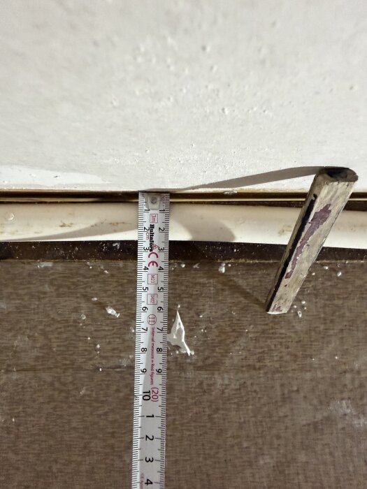 Målestok mod en væg og gulv, viser ca. 7 cm. Bruges til at planlægge konstruktionen af en sokkelliste med dimensionerne beskrevet i teksten.