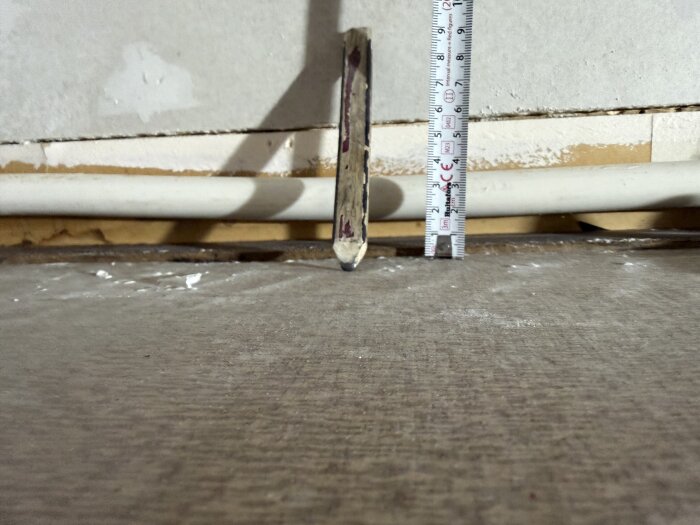 En opmåling af rørplads langs en væg med en målepind og lineal, der viser afstand og dybde for potentielt at installere egne sokkellister.