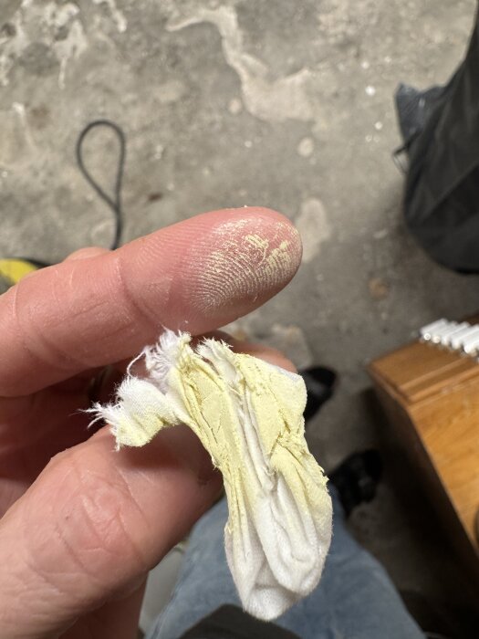 Finger gnuggar gulaktig färg på vit trasa för test av genomsläpplig färg.