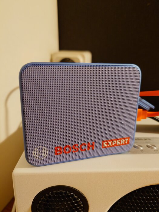 Blå högtalare med texten "Bosch Expert" på framsidan, placerad ovanpå en annan enhet.