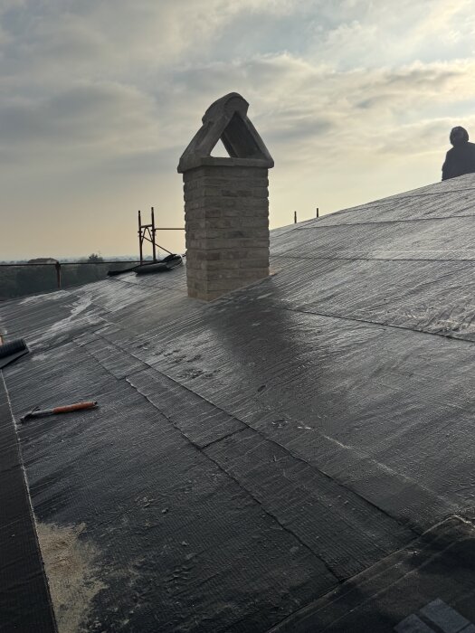 Tak under konstruktion med skorsten i förgrunden, verktyg synliga och en person i bakgrunden.