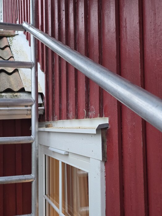 Fönster med nytt överbleck på röd träfasad, byggnadsställning synlig.