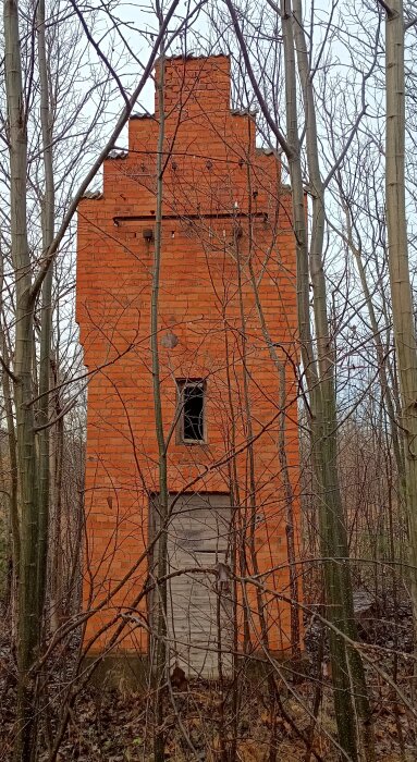 Äldre, övergivet transformatortorn i röd tegel nära Husby Rekarne kyrka, omgärdat av träd och grenar.