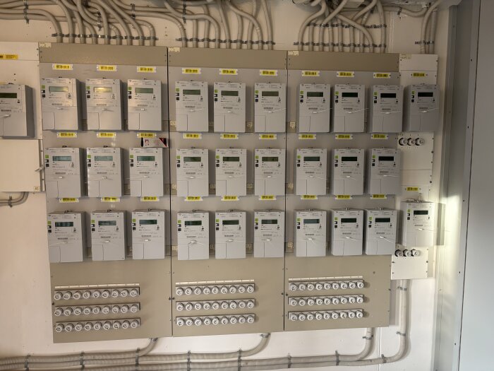 Elskåp med flera digitala elmätare och säkringar placerade under varje mätare. Mätaren i fokus är andra från vänster högst upp.