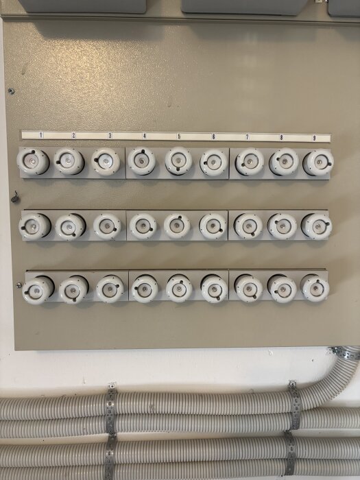 En elcentral med flera vita kopplingssäkringar i rader. Mätare markerad som den andra från vänster överst. Grå plaströr under säkringspanel.
