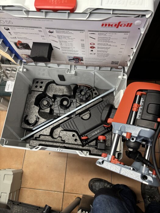 Mafell fräsmaskin i öppen verktygslåda med tillbehör, inklusive kopieringar och dammupptagningsutrustning, synlig på ett kaklat golv.