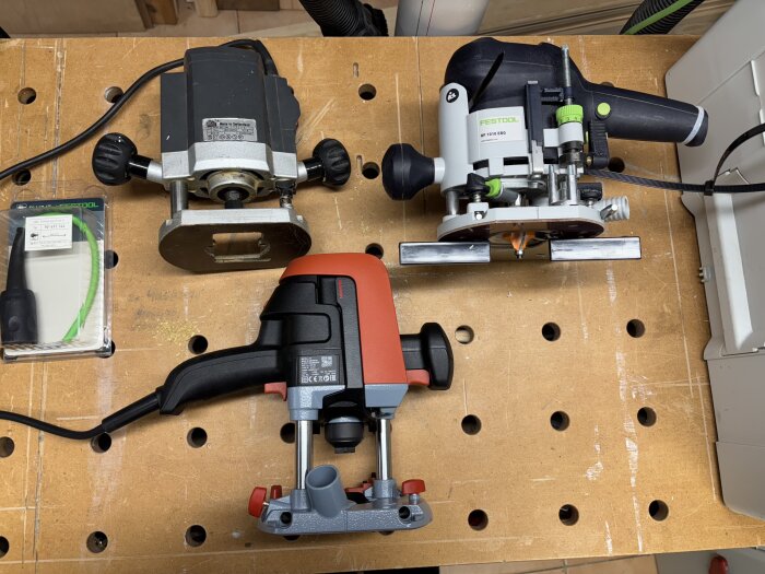 Tre mellanfräsar av märkena Elu, Festool och Mafell ligger på ett arbetsbord, tillsammans med ett paket tillbehör.