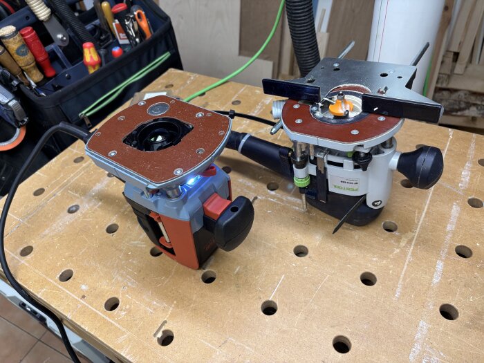 Två mellanfräsar, en Mafell och en Festool, på arbetsbänk med verktyg i bakgrunden.