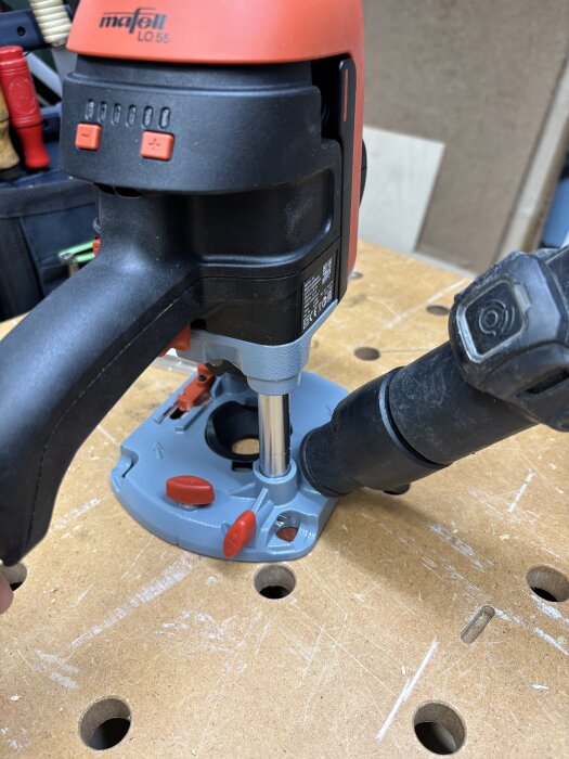 Mafell LO 55 fräs med dammsugarslang fäst vid basen står på en arbetsbänk med flera hål.