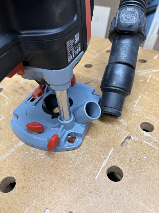 Närbild av en mellanfräs med dammutsug på ett arbetsbord, dammsugarslang ansluten och inställningsknappar i rött synliga.