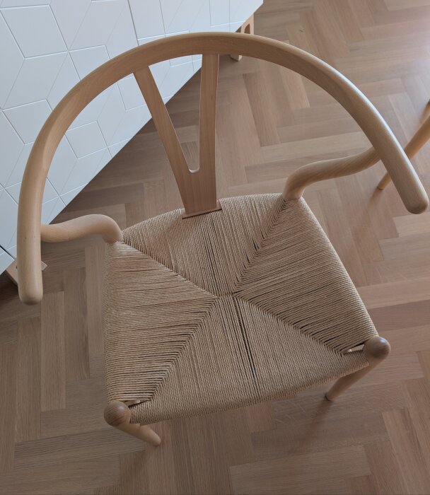 Y-stol i trä med flätad sits, fotograferad uppifrån. Den visar en något gulnad yta på ryggstödet. Ljusa och skuggade delar syns.