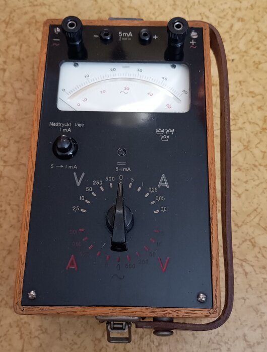 Kronstämplad multimeter tillverkad av LM Eriksson med träkanter och analoga visare för mätning av spänning och ström.