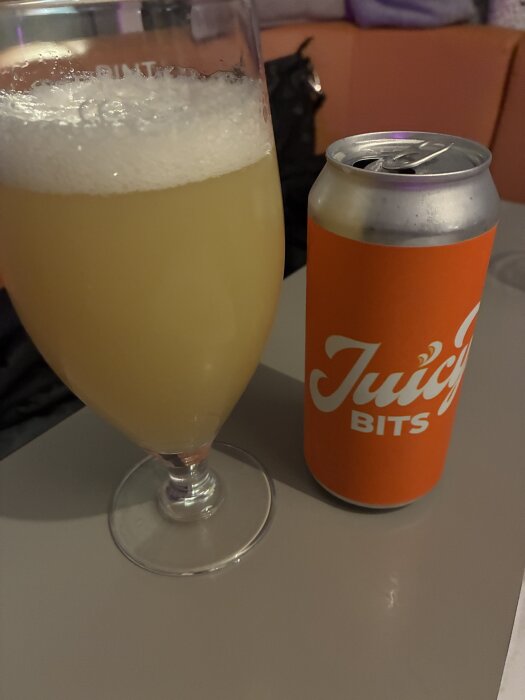 Ett glas med Hazy IPA bredvid en burk märkt "Juicy Bits" på ett bord.