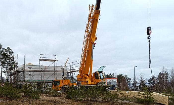 Byggarbetsplats med ett hus under stomresning, omgiven av byggnadsställningar och en gul lyftkran.