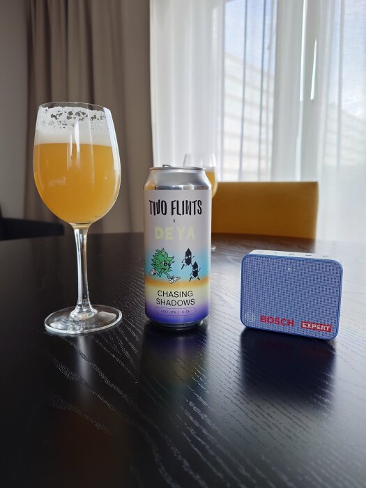 En burk "Two Flints x Deya Chasing Shadows" hazy IPA med ett glas öl och en Bosch Expert-enhet på ett bord.