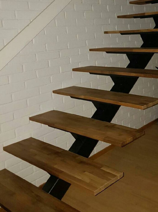 Inomhustrappa med svävande trästeg fästa på ett svart mittmonterat stålförstärkt rör mot en vit tegelvägg.