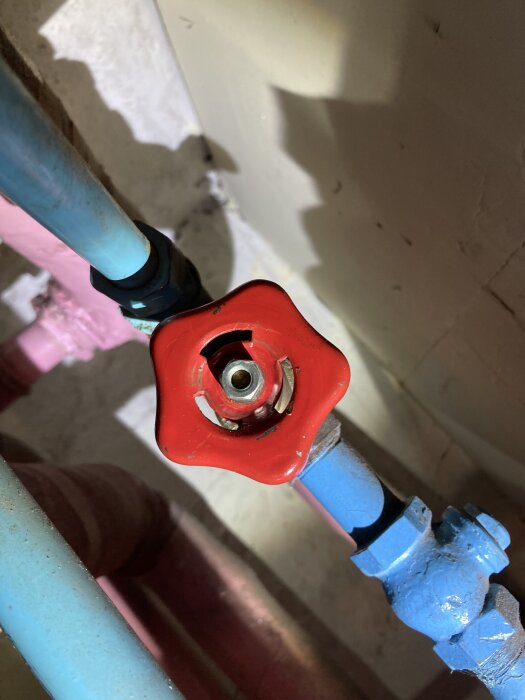 Röd ventil med intakt axel på blåmålat rörsystem, del av värmesystem, potentiellt trasig skjutmekanism.