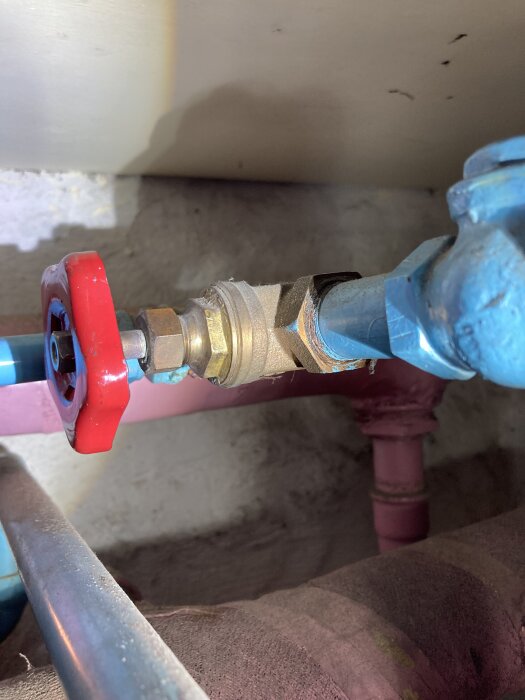 En trasig ventil med rött handtag i ett värmesystem, misstänks ha lossnat från skjutmekanismen, synlig rörkoppling till höger.