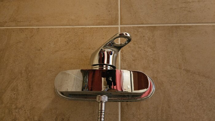 Gustavsberg duschblandare på beige kakelvägg, med en utåtgängad fattning där duschslangen tidigare satt fast.
