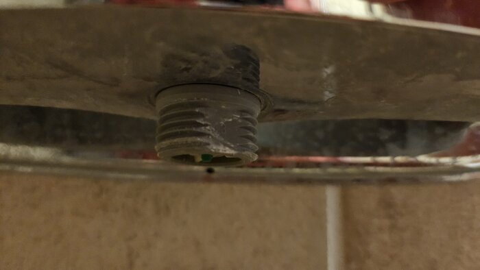 Närbild av en utåtgängad fattning på en Gustavsberg duschblandare där duschslangen tidigare satt, sedd underifrån.