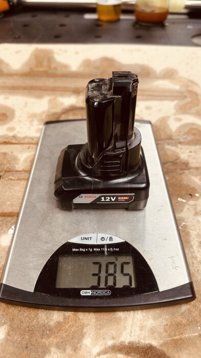 Bosch 12V 6.0Ah batteri vägs på en köksvåg som visar 385 gram.