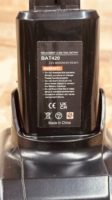 Bilden visar ett svart ersättningsbatteri, modell BAT420, 12V 8000mAh, med etikett "Made in China" och olika varningssymboler.
