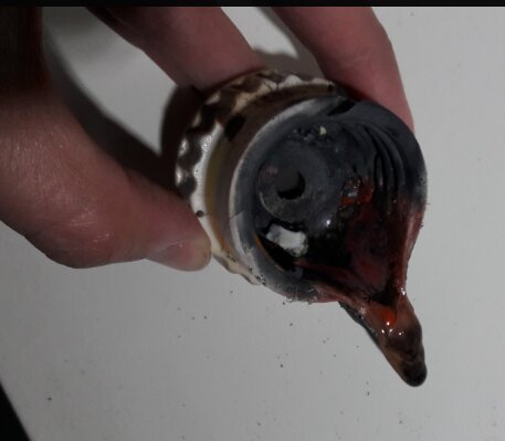 En hand håller ett bränt, smält stearinljus i en metallhållare på en vit bakgrund.