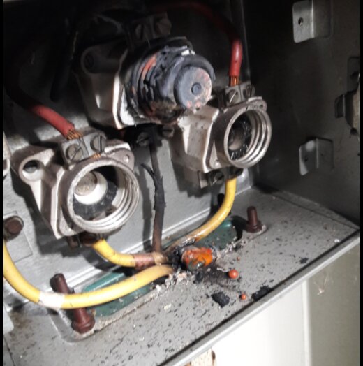 Skadad elektrisk komponent i en metallbox med ledningar, misstänkt brandskada och sot insidan.