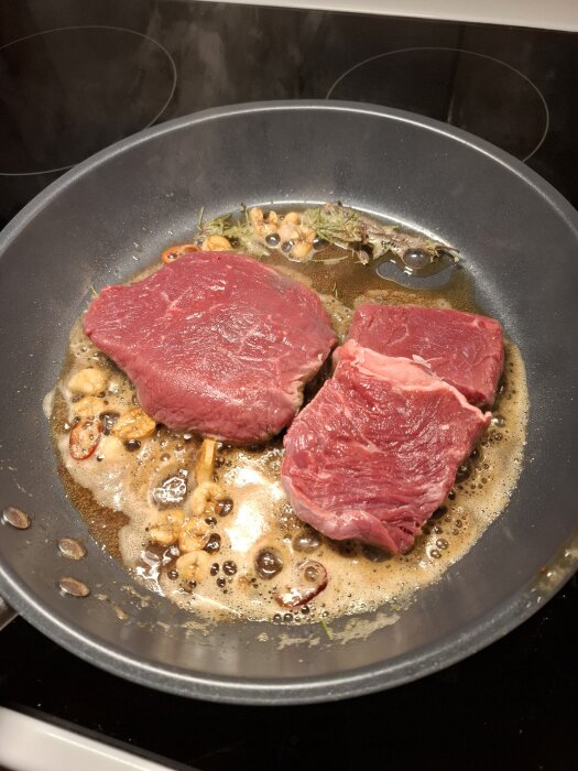 Två råa entrecote-skivor steks i smör med vitlök och örter i en stekpanna.