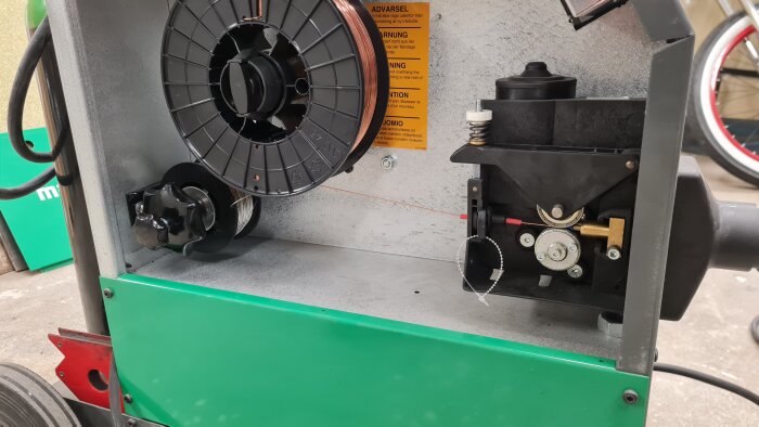 Hållare för svetstråd med stålspole, stjärnvred och låsdetaljer i en svetsmaskin.