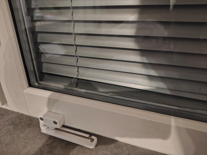 Inbyggda persienner i fönster som har släppt på ena sidan, med fokus på mekanismen och persiennens position.