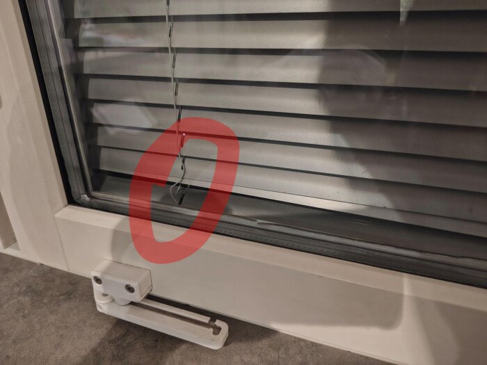 Inbyggd persienn i fönster med lös tråd på ena sidan, markerat med röd cirkel, visande problem med upphängning.