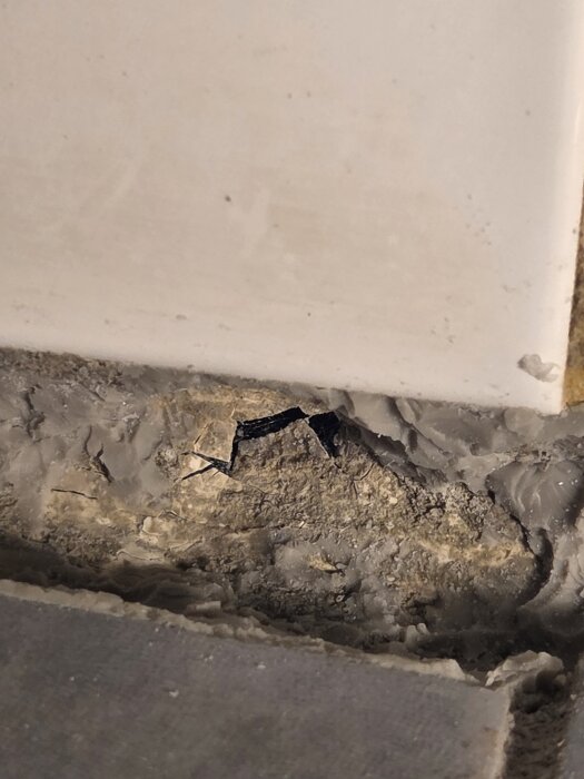 Hål i badrumsvägg mellan klinker och kakel, potentiellt genom tätskiktet, omgiven av silikonrester, synligt inne i duschområdet.