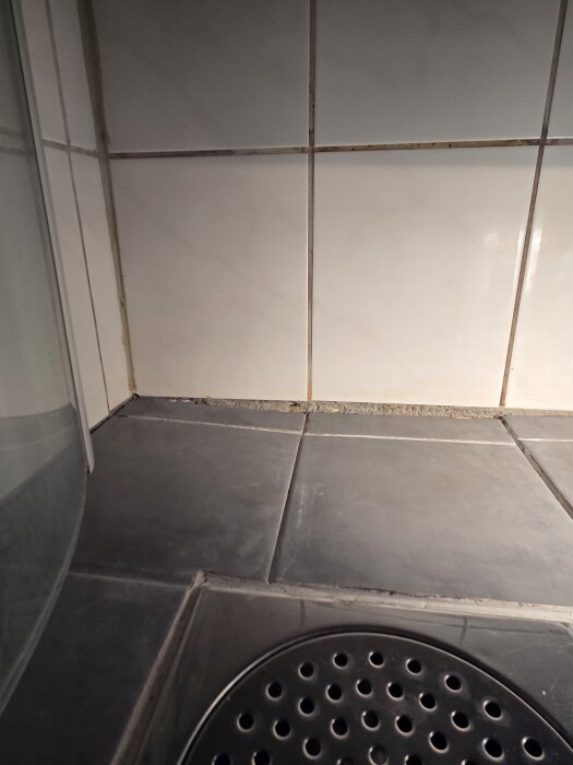 Hål i duschområde mellan kakel och klinker, synligt där silikon tidigare täckt. Nära golvbrunn, kanaler i plattorna med mörkad fog.