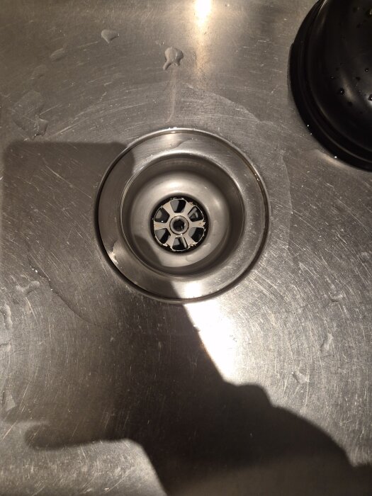 Diskbänk med närbild på ett rostfritt avlopp, där hålen verkar delvis blockerade.